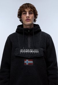 Sudadera de forro polar negro con capucha, que cuenta con un cuello con cremallera, un parche de logo texturizado y un acento de bandera noruega. Material suave y acogedor.