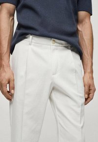 Białe spódnice klasyczne uszyte z teksturowanej tkaniny, z płaskim przodem, kieszeniami bocznymi i zapięciem na guzik. W zestawieniu z granatowym topem z krótkim rękawem.