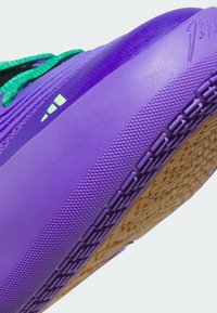 Fialová sportovní bota s texturovanou gumovou podrážkou, zelenými tkaničkami a minimalistickým designem. Má hladký svršek a vzor pro uchopení na podrážce.