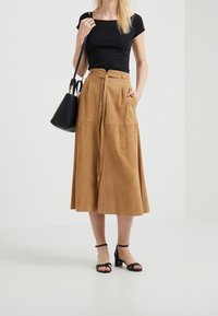 Brun mocka midikjol med en knytbelte, matchad med en figurnära svart topp och svarta ankelremsskor. En liten svart handväska fulländar looken.