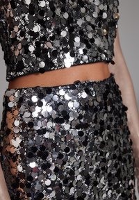 Mustavilla paljeteilla koristeltu kaksiosainen asu, johon kuuluu lyhyt toppi ja hame, jotka on kirkkaita ympyräisiä paljetteja, jotka heijastavat valoa.