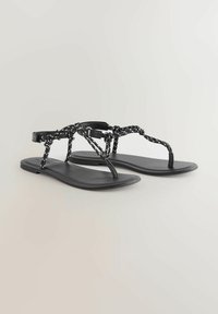 Black flat sandals featuring a textured strap design with white accents, a toe post, and a minimalist sole. Made from synthetic materials.