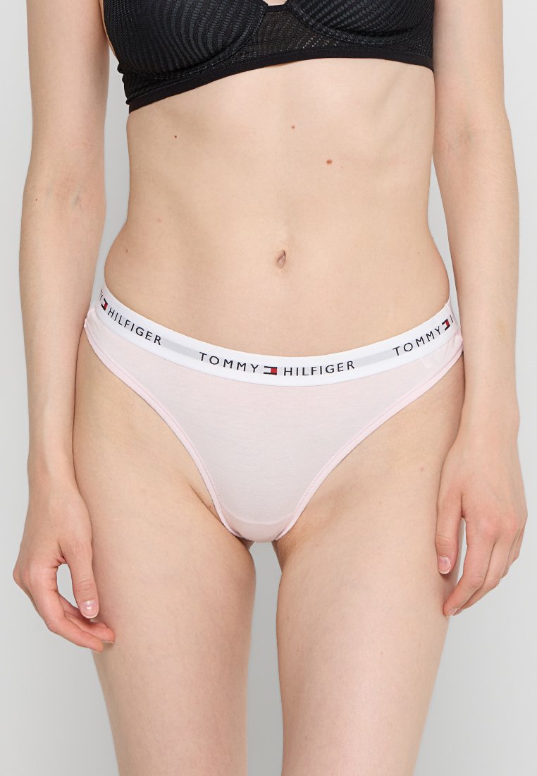 Tanga de algodón rosa con una cinturilla blanca que presenta el logo en negro de "TOMMY HILFIGER". Textura suave, diseño ajustado y cobertura mínima.