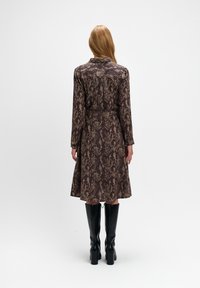 Brązowa sukienka w wężowy wzór z paskiem w talii, długimi rękawami i rozkloszowanym dołem, w zestawie z czarnymi botkami na wysokim obcasie do kolan.