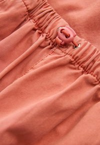 Pantaloni in misto cotone di colore corallo, caratterizzati da una vita elasticizzata con cordoncino regolabile e dettagli in hardware riflettente.