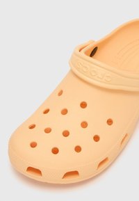 Peach-colored Crocs shoe with a perforated design, flexible material, and raised edging. Features a rounded toe and an adjustable back strap.