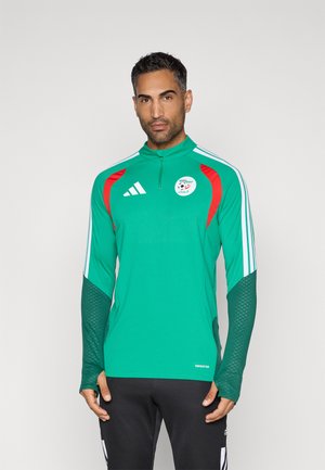 Zelený atletický dres s červenými akcentmi, zipsovým golierom a logom. Obsahuje štruktúrované rukávy a biele pruhy po stranách.