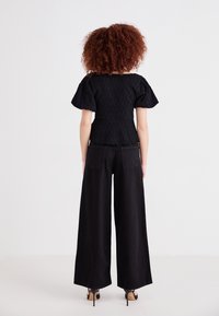 Top nero con texture e maniche a sbuffo abbinato a pantaloni larghi neri, con tasche posteriori e una vestibilità comoda. Scarpe con tacco alto.