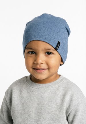 Young child wearing a light blue beanie and light gray sweatshirt, smiling and facing slightly toward the camera on a white background.
