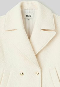 Manteau en laine couleur crème avec un design croisé, des revers à pointe et deux boutons dorés. Doublé d'un motif à rayures verticales subtil.