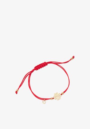 Czerwona pleciona bransoletka z metalowym złotym charmsa, który ma skomplikowany wzór kwiatowy oraz małą okrągłą zawieszkę, prezentującą błyszczące akcenty.