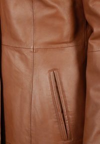 Bruine leren jasdetail met een verticale zak, een gladde textuur en op maat gemaakte naden met een getailleerd ontwerp.