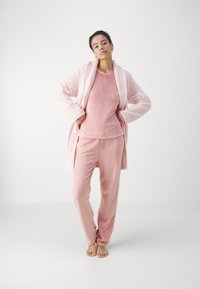 Conjunto de loungewear de forro polar rosa que incluye una bata, una camiseta de manga larga y pantalones. Textura suave con un corte relajado y detalles de costura mínimos.