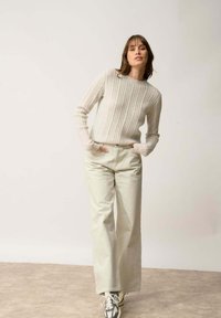 Vaaleanharmaa ribbineulepusero, jossa on pyöreä kaula-aukko. Yhdistetty leveälahkeisiin beigeihin housuihin ja vaaleisiin lenkkareihin. Rakenteellinen, rento asu.