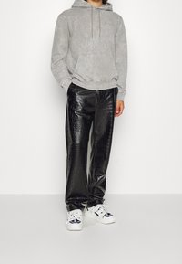 Felpa grigia con cappuccio e tasca frontale, abbinata a pantaloni neri in finta pelle di coccodrillo. Indossata con sneakers bianche con dettagli neri.