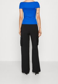 Top ajustado azul sin hombros combinado con pantalones cargo anchos negros que cuentan con bolsillos laterales y una textura suave.