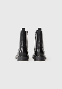 Black leather ankle boots with a glossy finish, zip closure, and a low heel. Features stitched seams and pull tabs at the back.