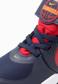 Korisne košarkaške cipele s gornjim dijelom od tamnoplave sintetike, crvenim mrežastim jezikom i crnim vezicama. Sadrže okrugli logo s natpisom "TEAM HUSTLE" na gležnju.