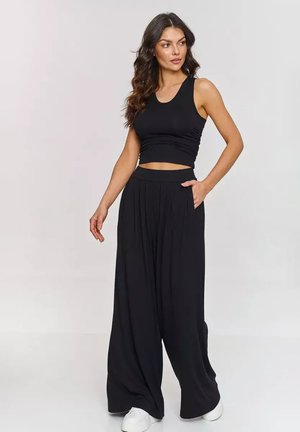 Czarny crop top o dopasowanym fasonie, w połączeniu z szerokimi czarnymi spodniami z zaszewkami i kieszeniami, noszony z białymi trampkami.