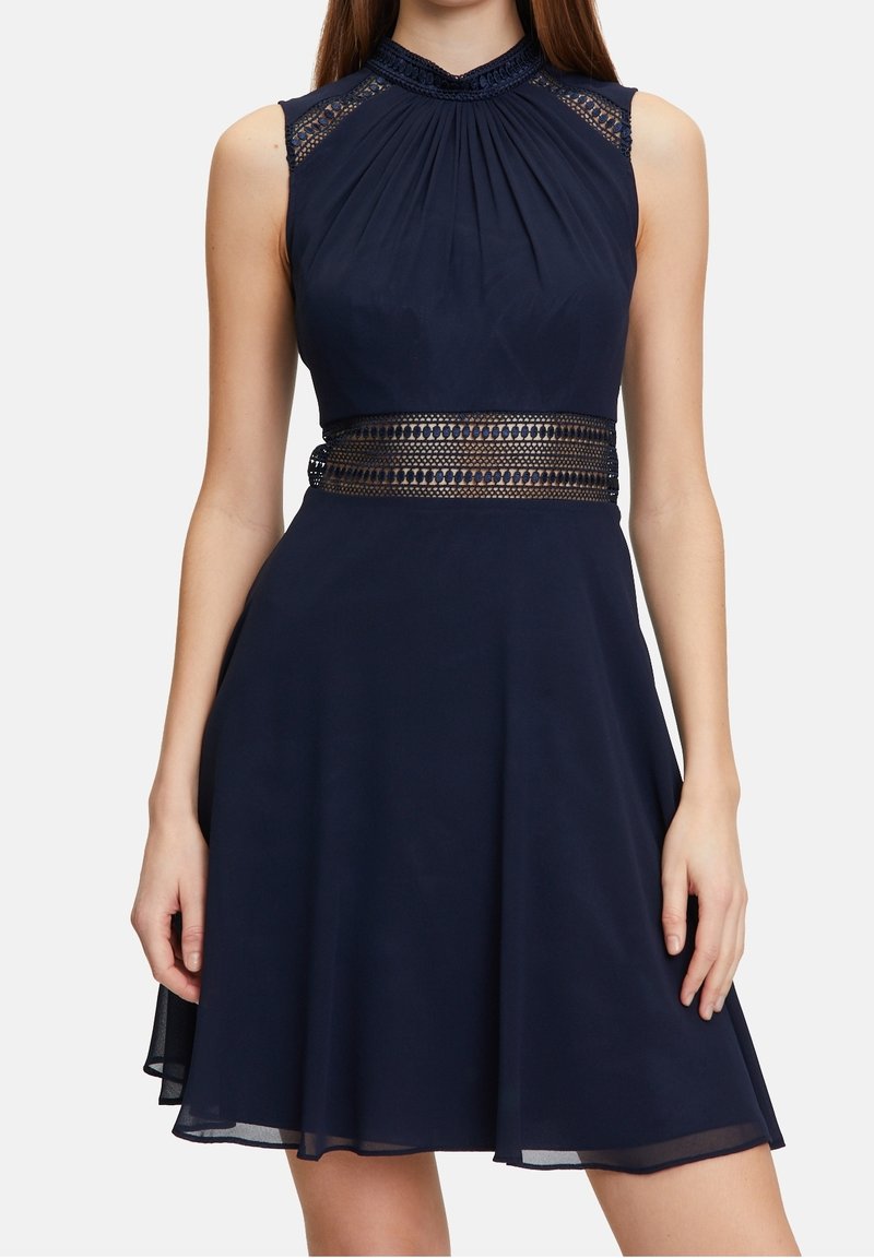 Mörkblå ärmlös klänning med plisserad liv, spetsdetaljer vid axlarna och en texturerad midje-design. Utskuren kjol.