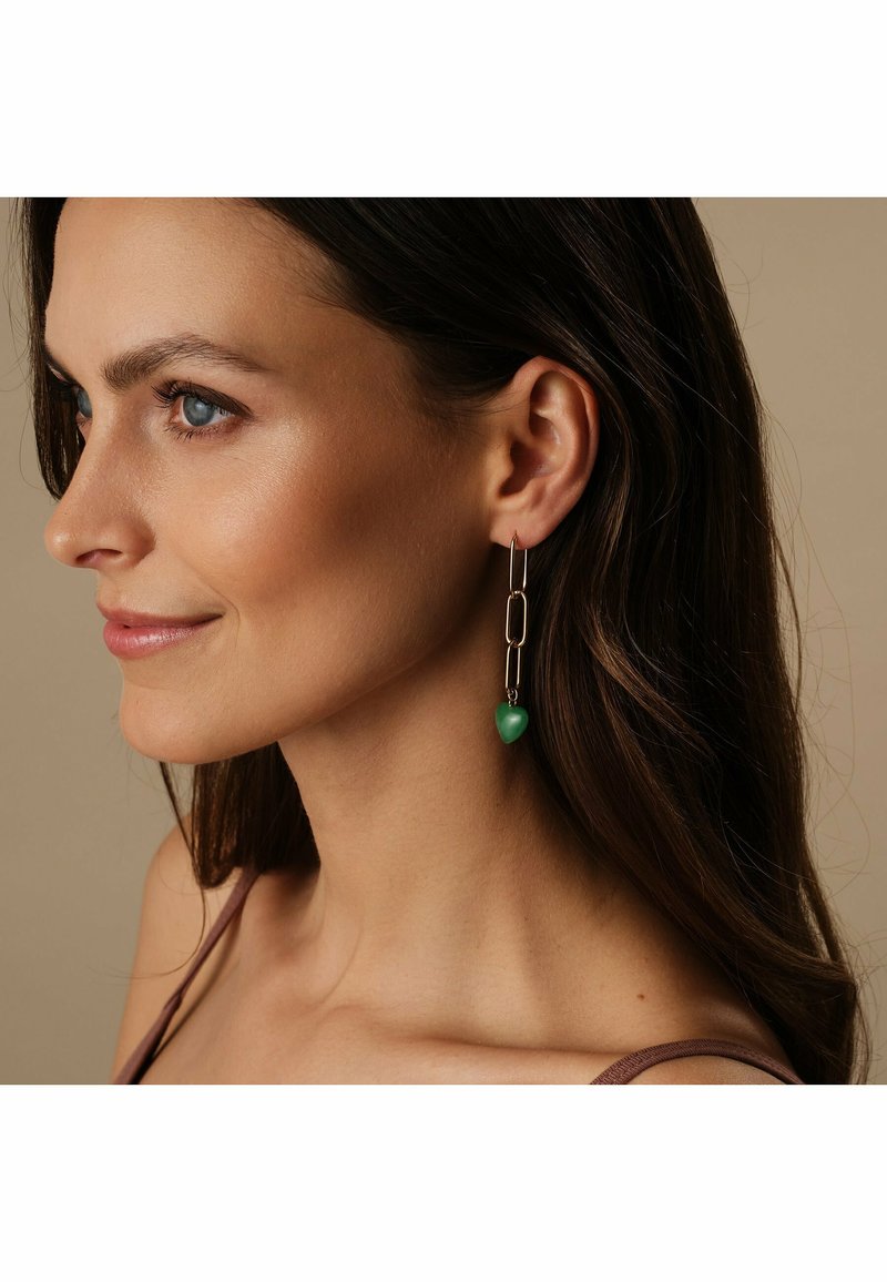 Boucles d'oreilles ton or présentant un design à chaîne liée avec un accent en forme de cœur vert. Légères et allongées, adaptées à diverses occasions.