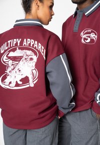 Bordeauxroter Pullover mit grauen Ärmeln; zeigt auffällige weiße Grafiken eines Hundes und den Text "MULTIPLY APPAREL." Weicher Stoff, lockere Passform.