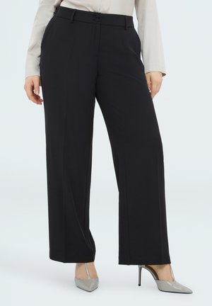 Sorte bukser med vide ben, to knapper og sidelommer, båret med beige skjorte og grå spidse hæle.