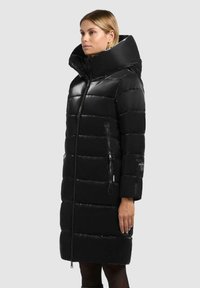 Lange zwarte pufferjas met een hoge kraag, glanzende afwerking, rits aan de voorkant en zijzakken. Bevat horizontaal gestikte secties en logodetail.