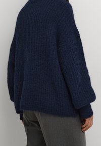 Granatowy sweter wykonany z teksturowanego dzianinowego materiału, charakteryzujący się luźnym krojem, szerokimi rękawami i wysokim dekoltem. Dodatki to ściągacze na rękawach.