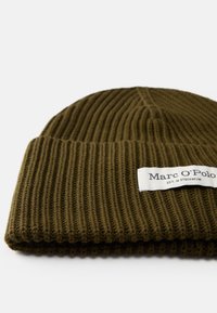 Gorro de malha em verde oliva com textura canelada e dobra na aba. Apresenta um rótulo branco com texto preto na frente.