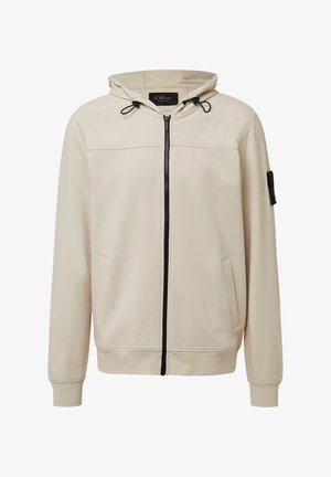 Beige Zip-Hoodie mit einer Kordelzugkapuze, zwei Seitentaschen, gerippten Bündchen und einem kleinen schwarzen Stoffpatch am Ärmel. Glatte Textur.