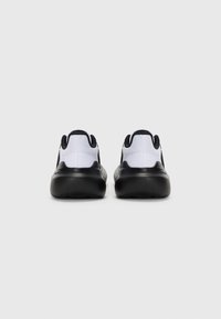Des chaussures de sport noires et blanches au design lisse et arrondi, avec une tige texturée et des semelles noires rembourrées.