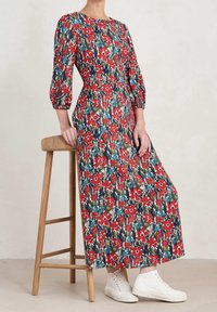 Robe maxi avec un corsage ajusté et des manches bouffantes, arborant un motif floral vibrant dans des tons de rouge, bleu et vert sur un fond sombre.
