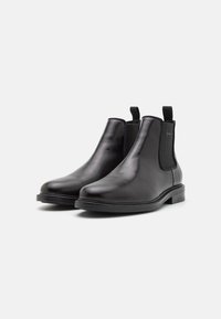 Black leather Chelsea boots with elastic side panels, round toe, pull tab, and flat rubber sole. Smooth texture with minimal design accents.