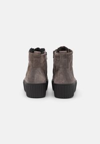 Para brązowych zamszowych botków za kostkę z czarną grubą ryflowaną podeszwą i czarnym fleece'em wewnątrz, widocznych z tyłu na białym tle.