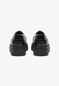 Zapatos de cuero negro con punta redondeada, tacones bajos y suelas de goma texturizadas. Presentan detalles de costura y un acabado suave.