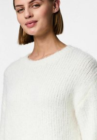 Vit ribbad tröja med avslappnad passform, rund halsringning och mjuk, fluffig textur. Framträdande stickat mönster över hela tyget.