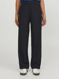 Marineblauwe wijde broek in synthetische stof met riemlussen, twee zijzakken en een gladde textuur. Gecombineerd met witte en grijze sneakers.