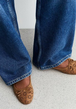 Bruine geperforeerde leren ballet flats met een strik; wijde donkere blauwe denim jeans; lichte gestructureerde vloer achtergrond.