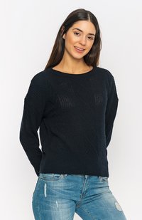 Marineblau gestrickter Pullover mit einem strukturierten Rautenmuster, rundem Ausschnitt und langen Ärmeln, kombiniert mit hellblauen, verwaschenen Jeans.