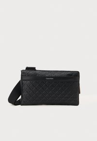 Sort quiltet crossbody taske med et struktureret mønster, justerbar rem og et frontlogo panel. Fremstillet af syntetisk læder.