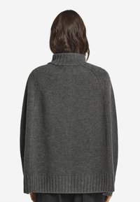 Grå oversized tröja med hög krage och ribbad nederkant. Tillverkad av ett strukturerat stickat material, den har raglanärmar.