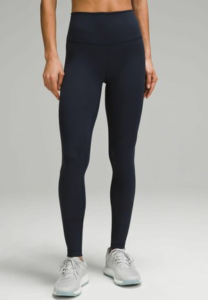 High-waisted, navy leggings made of stretchy material, fitted design with smooth texture, paired with light gray athletic shoes.