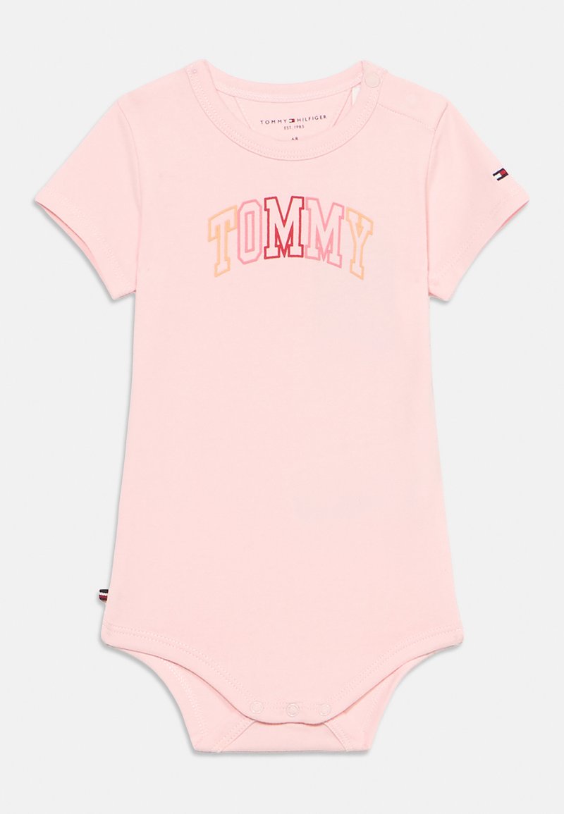 Ροζ κορμάκι με κοντά μανίκια από απαλό ύφασμα, με τη λέξη "TOMMY" σε πολύχρωμα γράμματα. Κουμπώματα στον λαιμό και στην κάτω πλευρά.