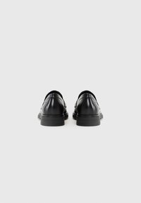 Scarpe in pelle nera con finitura liscia, punte arrotondate e tacco basso a strati. Dettaglio di cucitura sottile lungo i bordi.