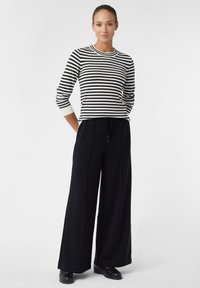 Maglione a righe in bianco e nero, con maniche lunghe e scollo rotondo, abbinato a pantaloni neri a gamba larga. Tessuto liscio, vestibilità casual.