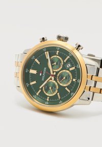Ανδρικό ρολόι χειρός με πράσινο καντράν, χρυσή στεφάνη, τρεις υποκαντράν, παράθυρο ημερομηνίας και δίχρωμο μεταλλικό μπρασελέ.
