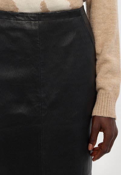 Gonna in pelle nera con una texture liscia e un design aderente. Presenta un taglio dritto e una leggera brillantezza, abbinata a un maglione di colore chiaro.