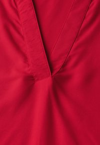 Tessuto rosso con design a V; texture liscia con dettagli di cucitura diagonale vicino al colletto.