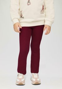 Bordeaux geribbelde leggings gecombineerd met witte en roze sneakers, gedragen door een kind in een crèmekleurige trui met dierenprints.